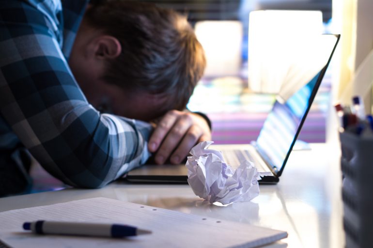Man met writer's block legt z'n hoofd op laptop. 