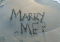 Foto van de geschreven tekst 'marry me?' in het zand.