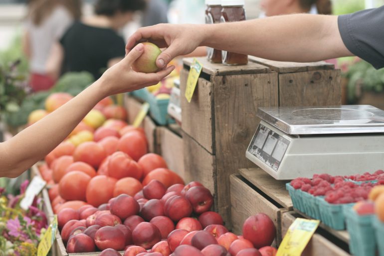 Foto van een marktkoopman die een appel geeft aan een klant. Een voorbeeld van een klantgerichte organisatie.
