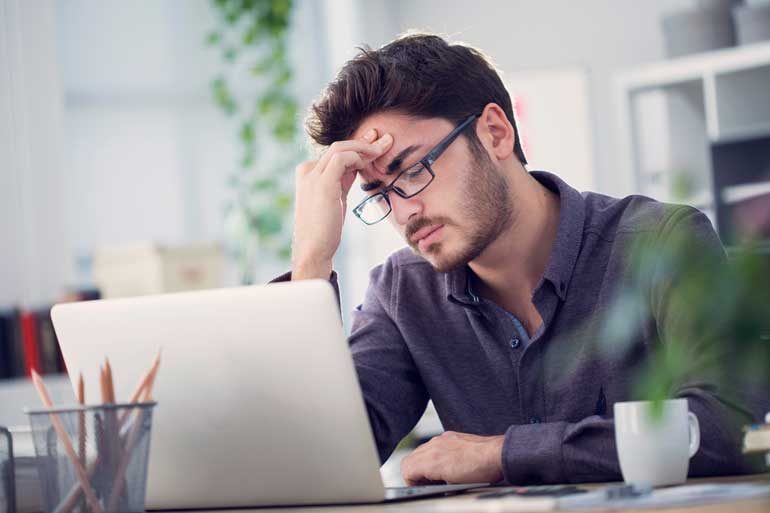 Man heeft hoofdpijn bij laptop.