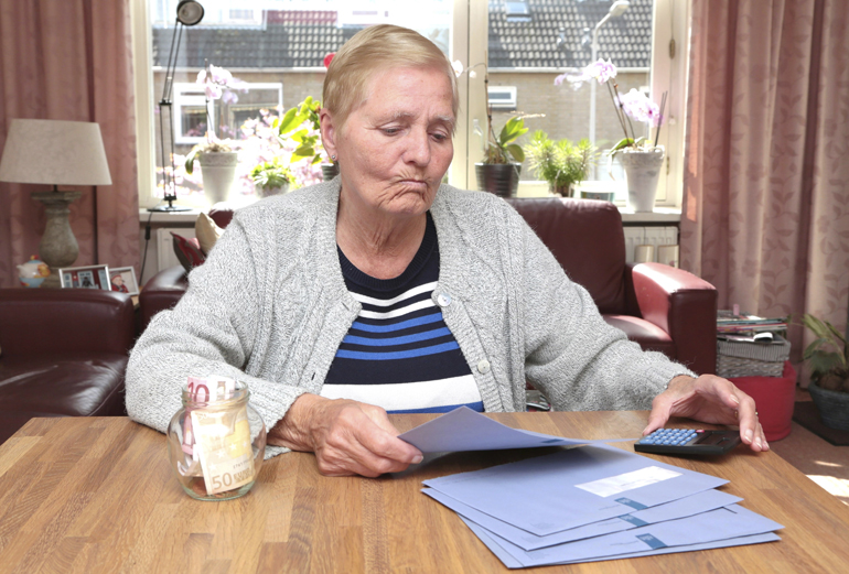 Oudere vrouw kijkt sip naar stapeltje blauwe brieven van de belastingdienst.
