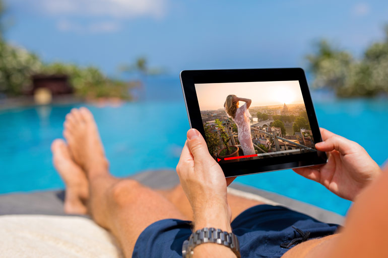 Man ligt aan het zwembad, kijkt Netflix op tablet.