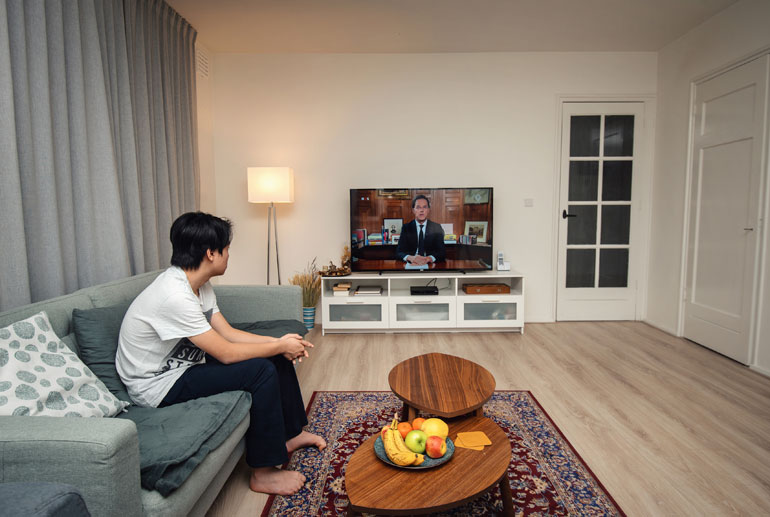 Jongen kijkt naar historische corona-toespraak van Mark Rutte op tv.