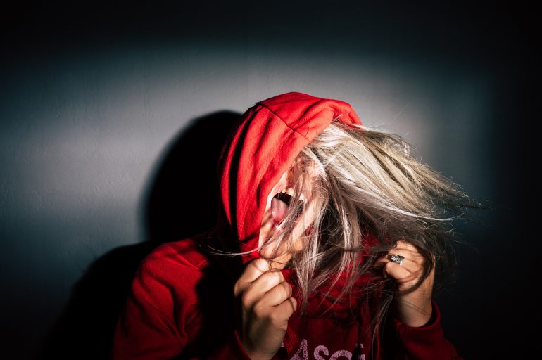Foto van jonge vrouw met rode hoodie die het uitschreeuwt van frustratie