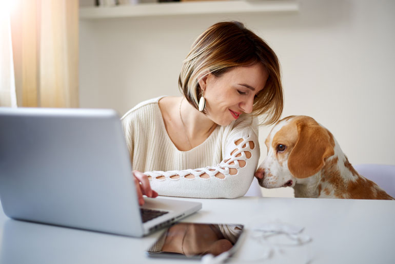 Vrouw werkt thuis met laptop en hond.