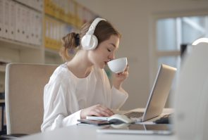 Vrouw met koptelefoon op drinkt koffie achter laptop.