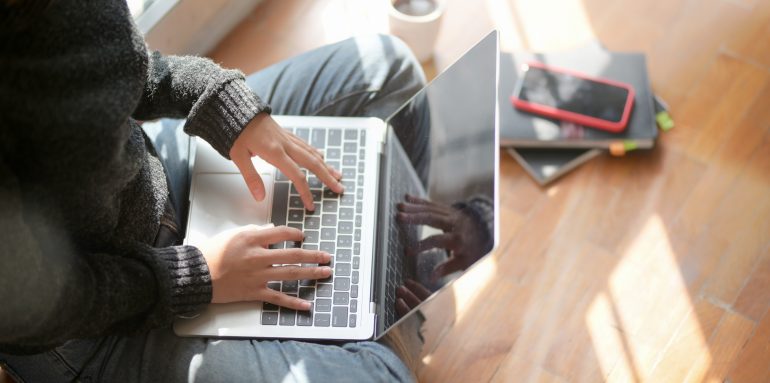Met laptop op de grond zittend werken thuiswerken.