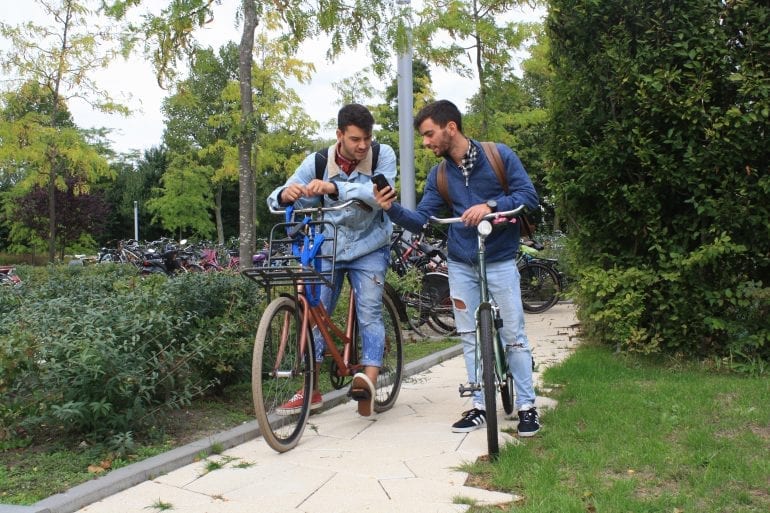 Twee studenten kijken naar hun mobiel op de fiets. Foto via Hogeschool Rotterdam.