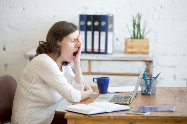 Vrouw gaapt bij haar laptop.