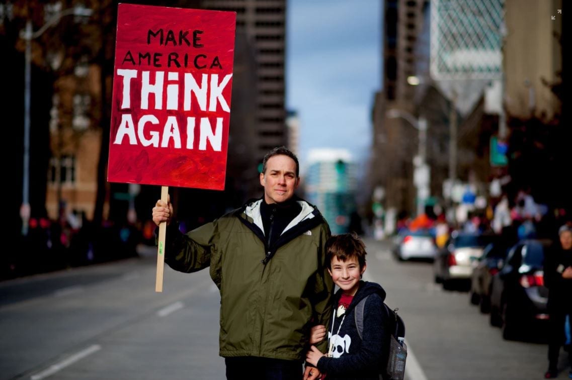 Man met een bord met de tekst 'Make America think again'.