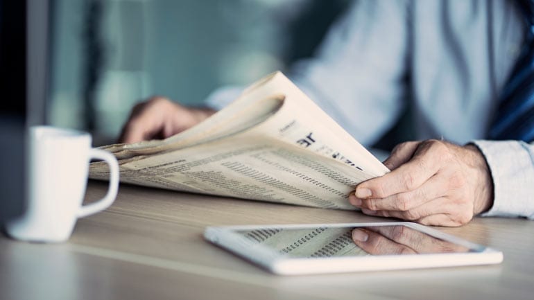 Man leest krant met kopje koffie.