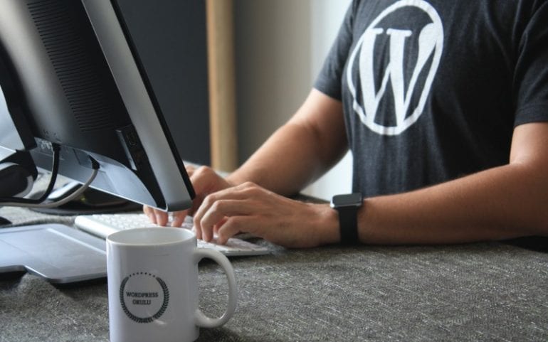 Bureau met monitor koffiemok en man in t-shirt met WordPress-logo en smartwatch