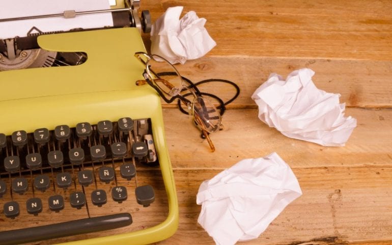 Typemachine op houten tafel met proppen papier en leesbril ernaast