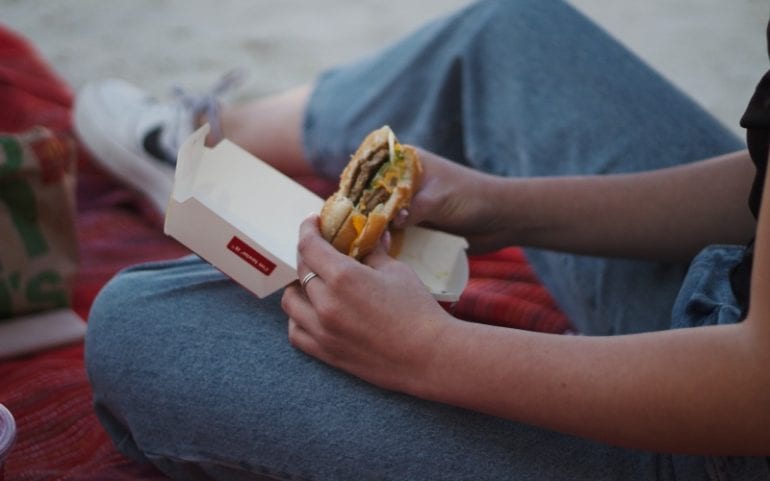 Persoon in spijkerbroek houdt burger McDonalds vast