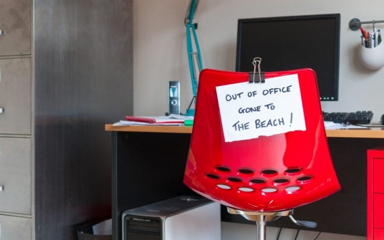 Bureau met briefje out of office en naar het strand
