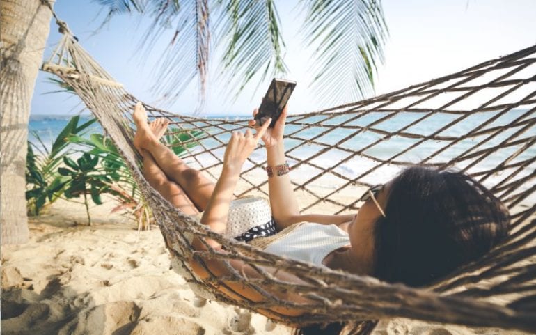 Vrouw in hangmat op strand kijkt op smartphone