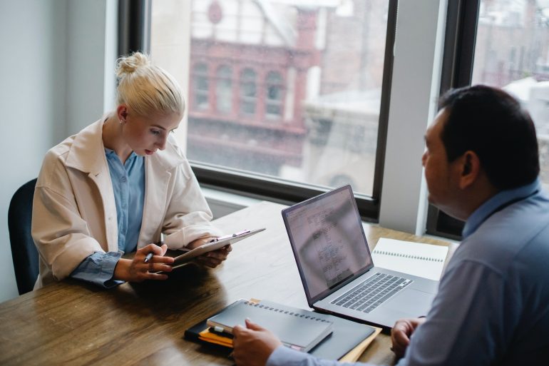 Foto van twee personen in gesprek, met een tablet respectievelijk laptop voor zich