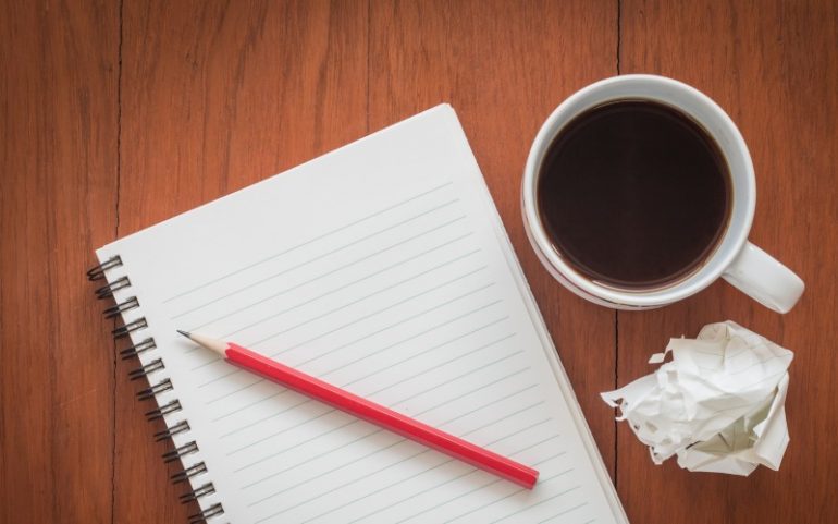 Notitieboek met potlood kop koffie en prop papier bij artikel over zakelijke duidelijke teksten schrijven