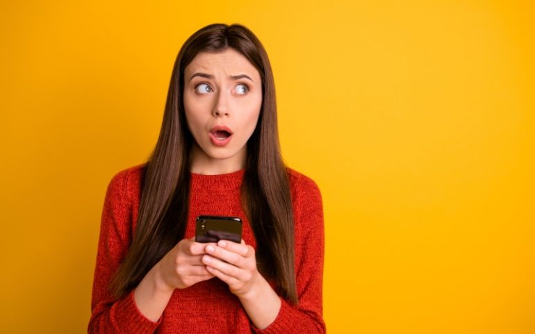 Vrouw met telefoon in haar hand kijkt verward ter illustratie van wachtwoord vergeten of bedenken