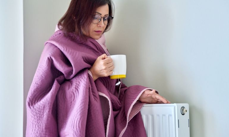 Vrouw heeft deken om en houdt haar hand bij de verwarming.
