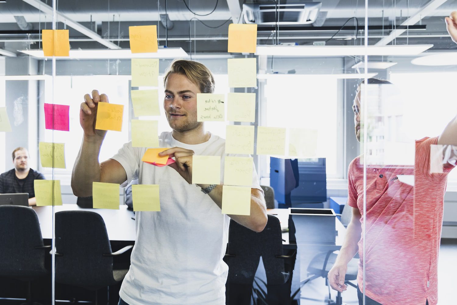 Mannen plakken post-its van customer journey op glazenwand