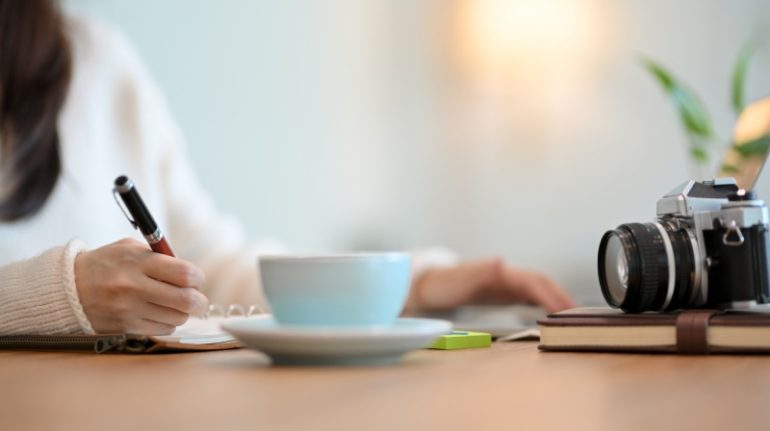 Beeld van vrouw die schrijft kop koffie en camera ter illustratie van klantcase schrijven