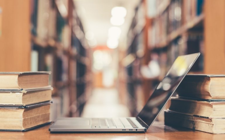 Laptop tussen boeken ter illustratie van boek schrijven