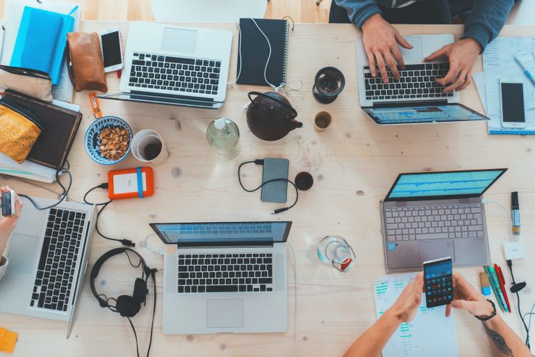 Bovenaanzicht van tafel met meerdere laptops en kantoorartikelen