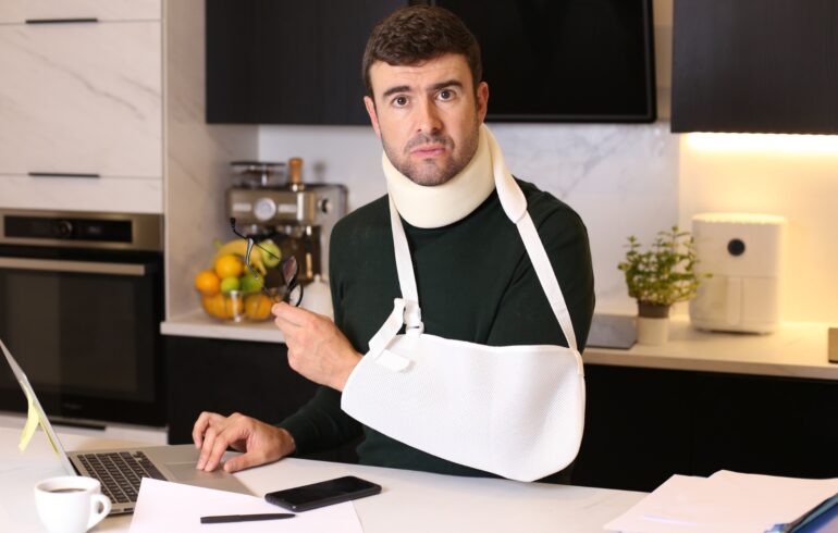 Man met gebroken arm in keuken achter laptop