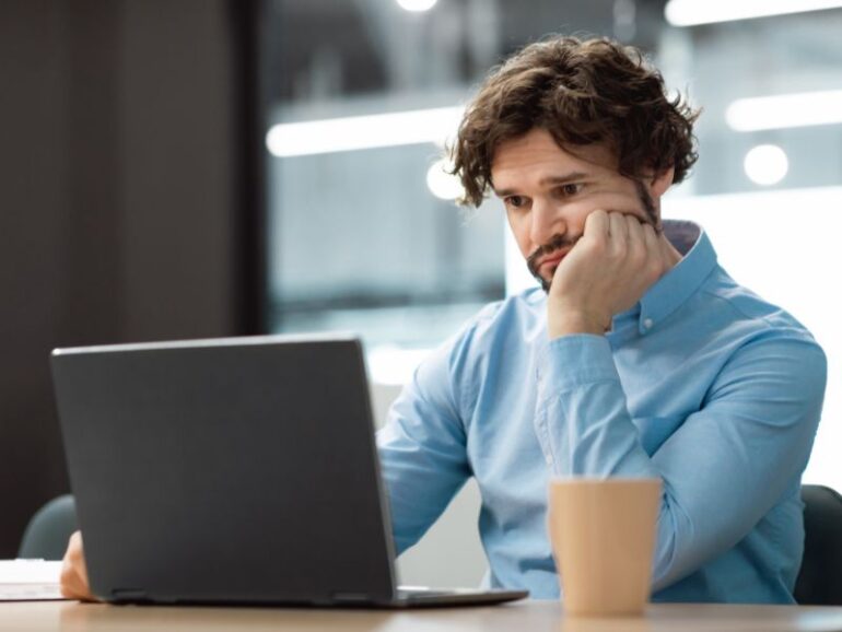 Een man achter een laptop die somber kijkt.