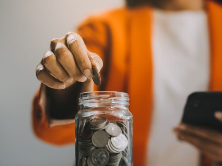 Een persoon stopt geld in een glazen potje. 