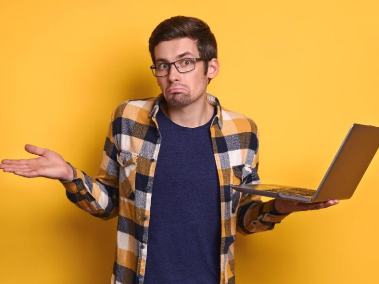 Een man met een laptop die vragend kijkt. 