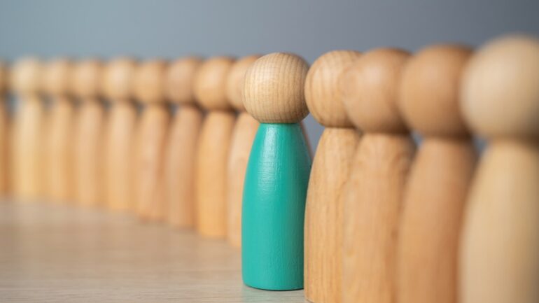 Houten pionnen op een rij waarvan een gekleurde ter illustratie van een leider - decoratief beeld bij artikel over meta-skills voor goed leiderschap