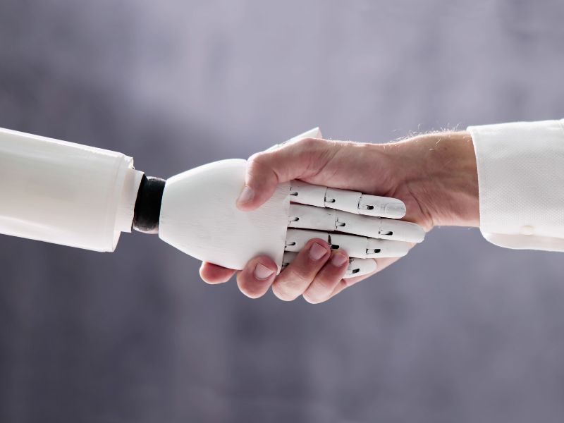 Robot hand en menselijke hand houden elkaar vast.