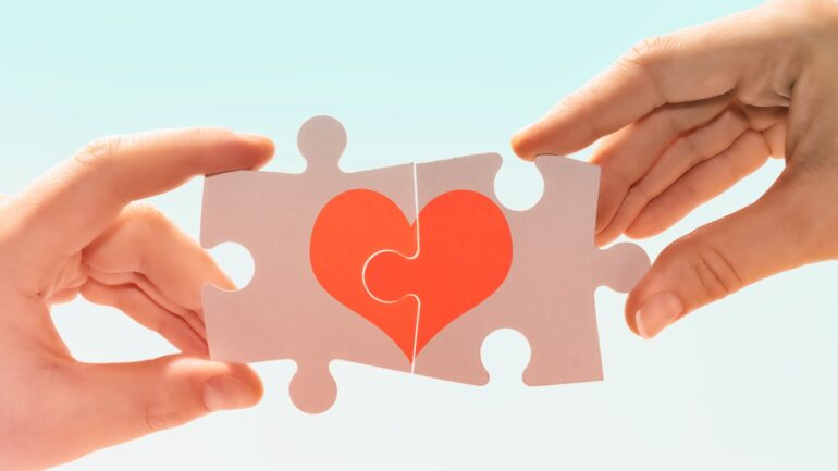 Handen die puzzelstukjes met hart samenvoegen ter illustratie van relatie als belangrijk marketingmechanisme