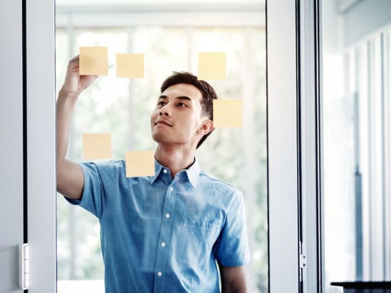 Een man hangt post-its aan een glazen muur. 