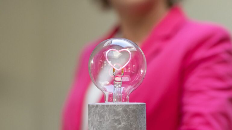 Decoratieve afbeelding van gloeilamp met hartje erin met op de achtergrond persoon in roze jasje