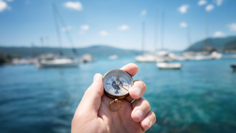 Decoratief beeld van hand met kompas met op de achtergrond de zee met boten
