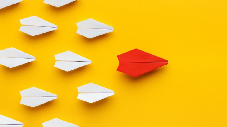 Papieren vliegtuigjes met een rood vliegtuigje voor op de groep.